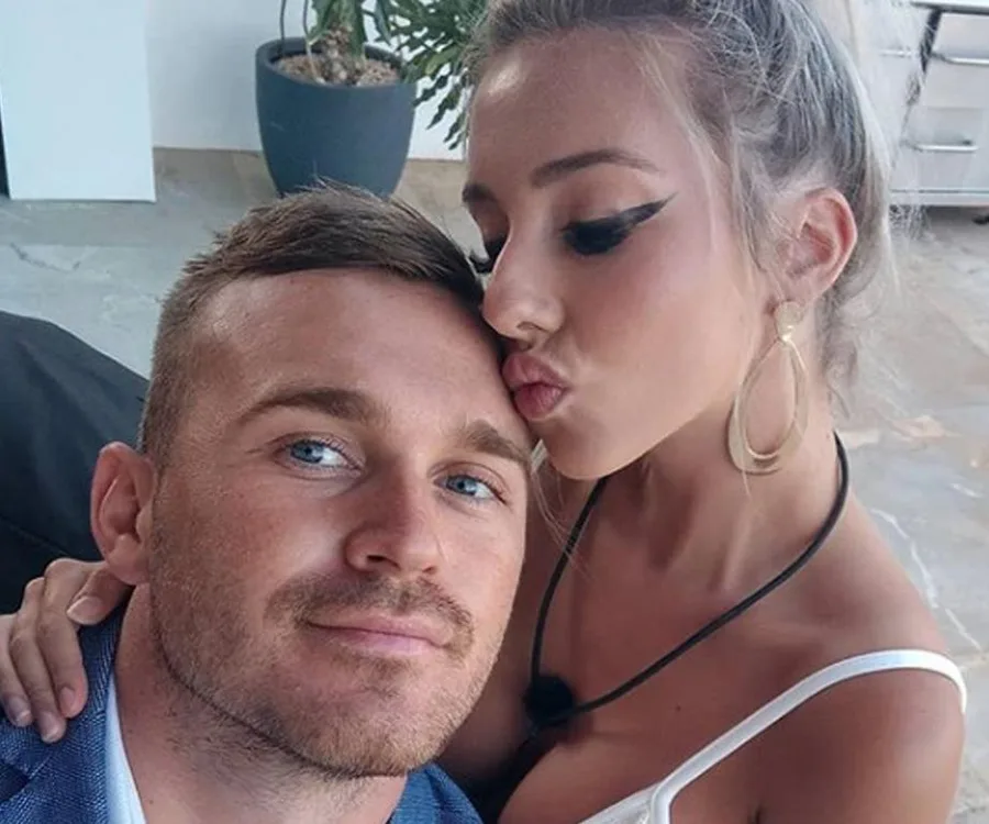 A couple taking a selfie; the woman leans in to kiss the man's forehead.