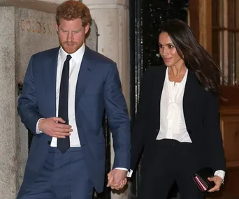 Couple holding hands, dressed formally; man in blue suit, woman in black suit with white blouse, walking together.