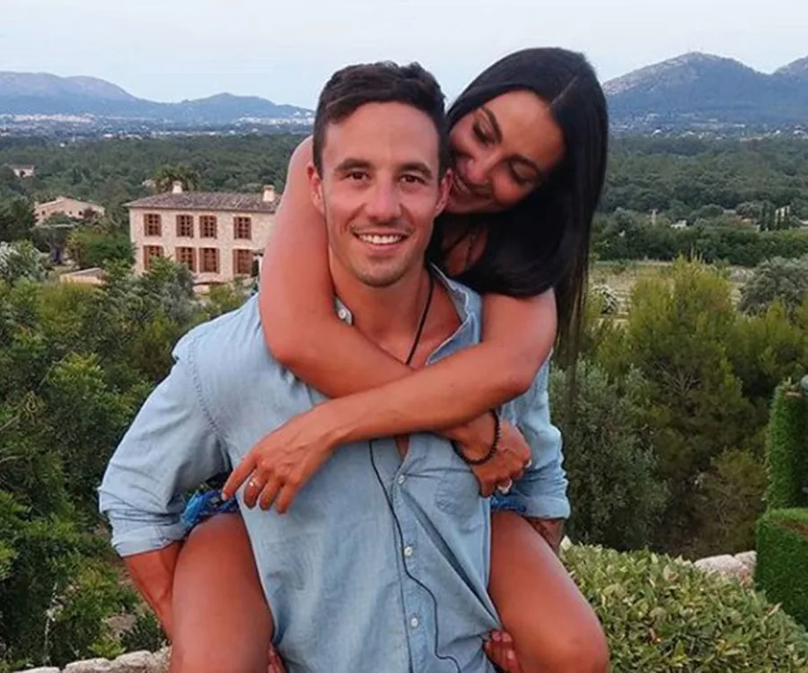 Man in denim shirt giving a woman a piggyback ride outdoors with scenic view in the background.