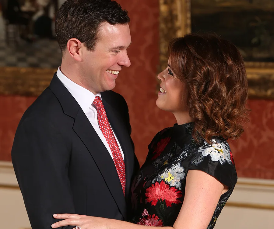 A couple smiling at each other in formal attire against an elegant background.