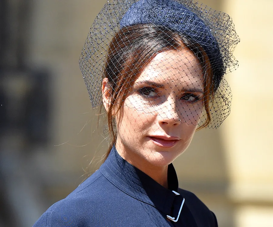 A woman in a navy outfit and matching hat with a netted veil looks directly at the camera.