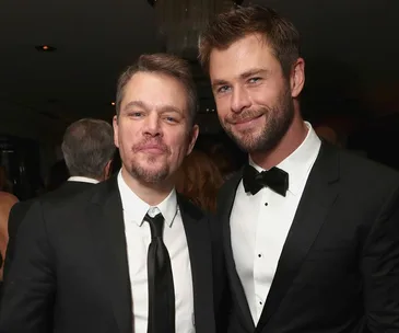 Two men in formal wear smiling at an event, one with a beard and bow tie and the other clean-shaven with a tie.