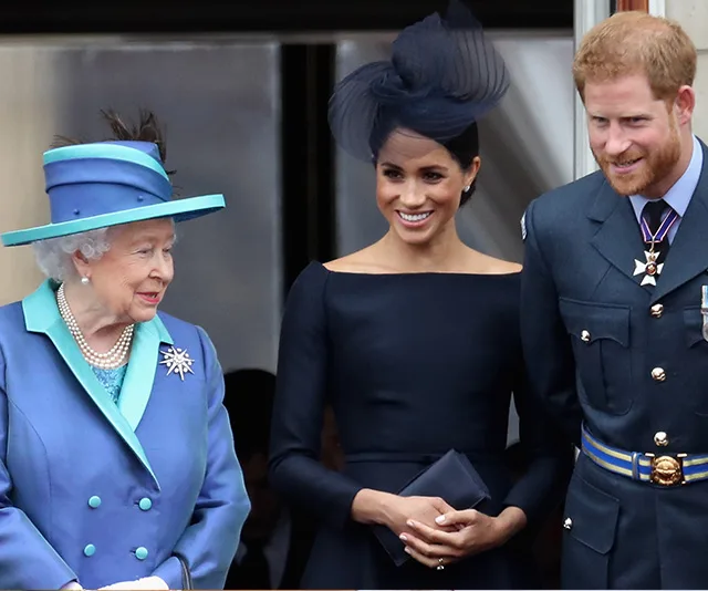 Queen Elizabeth II stands with Meghan Markle and Prince Harry, all smiling at a formal event.