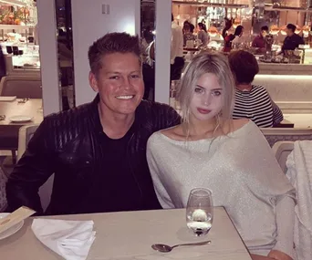 A smiling man and woman sit closely at a restaurant table; she wears a light sweater.