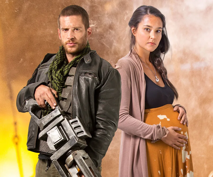 Dan Ewing and Rhiannon Fish in rugged outfits from "Occupation" movie, standing together against a dramatic background.