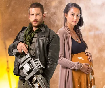 Dan Ewing and Rhiannon Fish in rugged outfits from "Occupation" movie, standing together against a dramatic background.