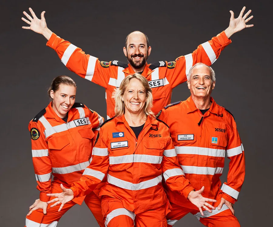 "Four people in orange SES uniforms posing together, smiling with arms raised."