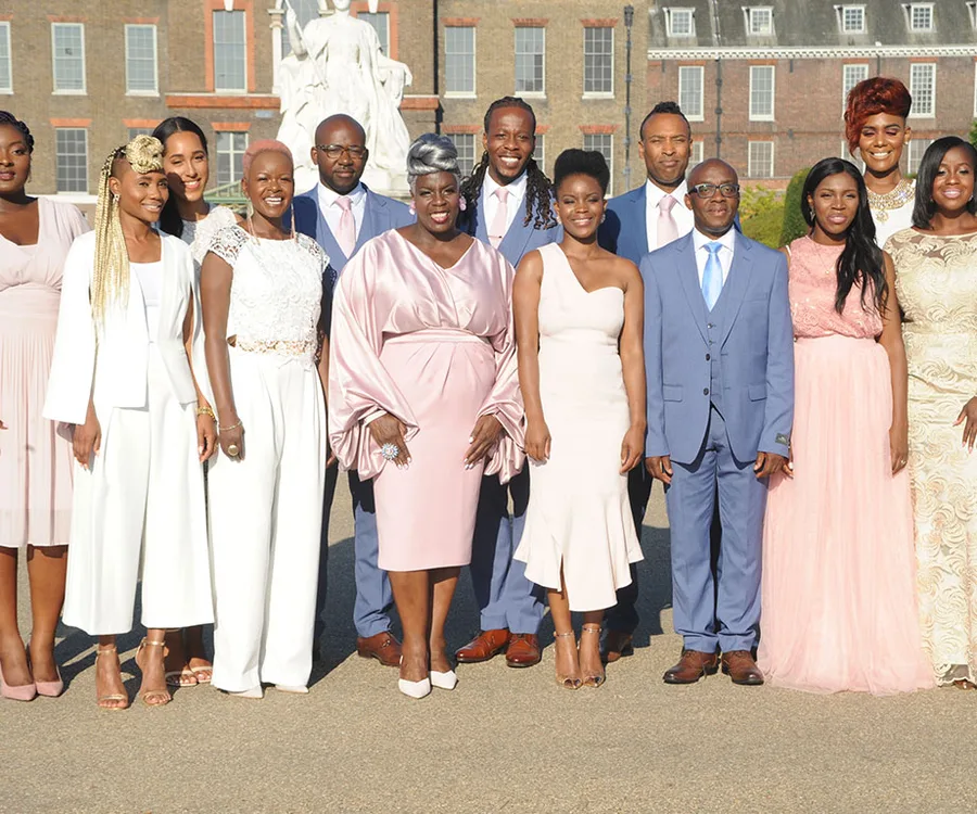 A diverse group of people in formal attire posing outdoors with a stately building in the background.