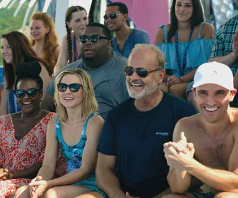 Group of people enjoying a sunny day, smiling and wearing sunglasses, with a beach setting.