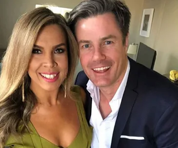 A smiling couple taking a selfie indoors, dressed in formal attire.
