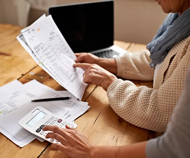 Person reviewing financial documents at a table with a calculator and laptop.