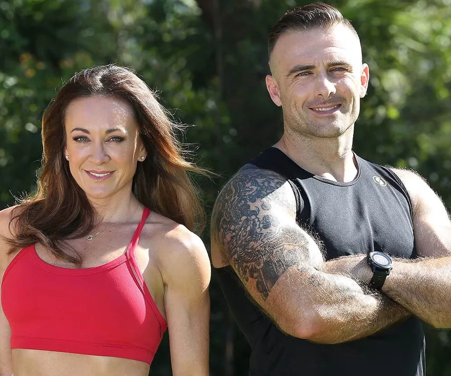 Two fitness trainers smiling, standing outdoors with crossed arms, one wearing a red sports bra, the other in a black tank top.