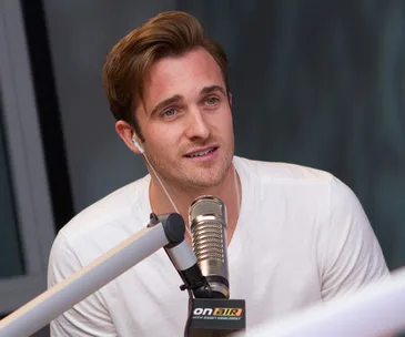 A man with earphones speaks into a microphone during a radio show, wearing a white shirt.
