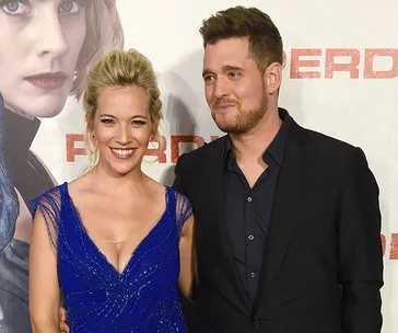 Couple smiling at a movie premiere, woman in a blue dress, man in a black suit.