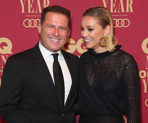 A couple smiling and posing at a red-carpet event with a "GQ Men of the Year" backdrop.
