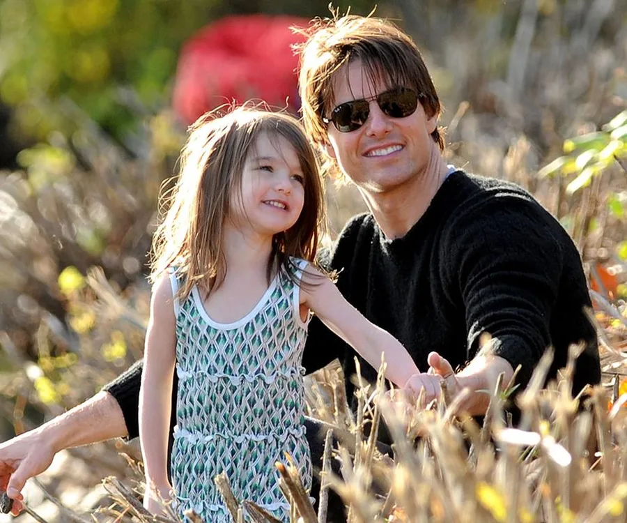 Father and daughter smiling and sitting outdoors amidst dry branches on a sunny day.