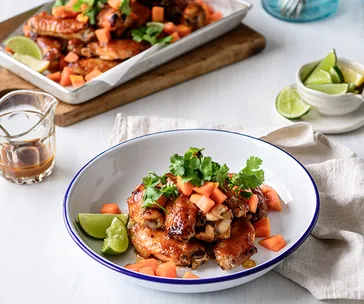 Sticky papaya chicken wings garnished with cilantro and lime wedges, served in a white bowl with fork beside.