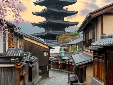 Traditional Japanese street with wooden houses and blooming cherry blossoms, featuring a pagoda at sunset.