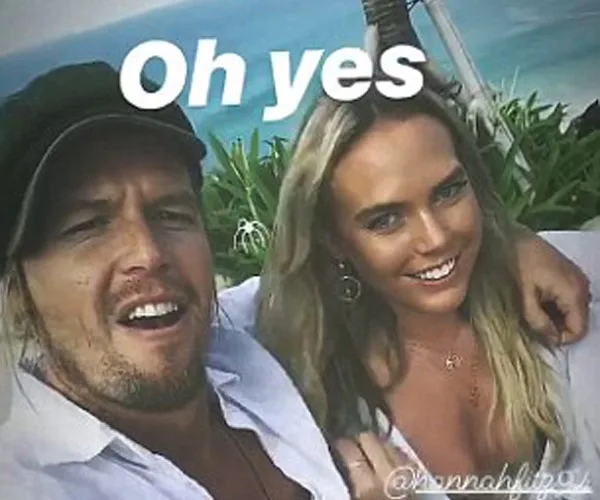 Two people smiling at the camera with the ocean in the background, text overlay "Oh yes".