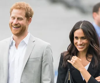 Couple smiling together, man in a gray suit and woman in a black outfit, walking outdoors.