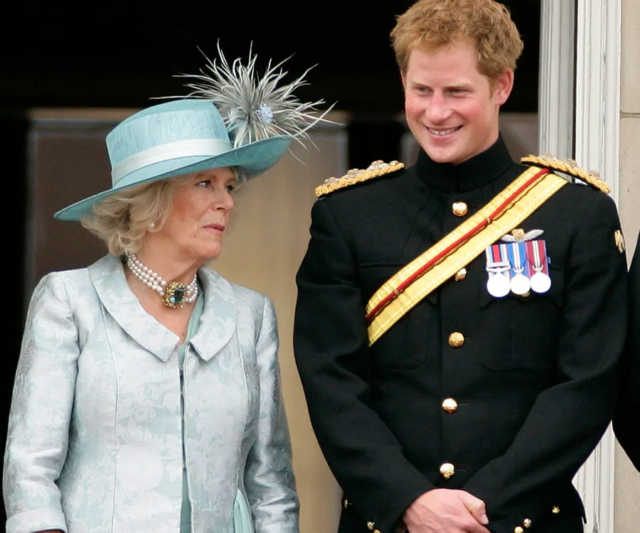 Two people smiling on a balcony, one in military dress, the other in a light blue outfit and hat.