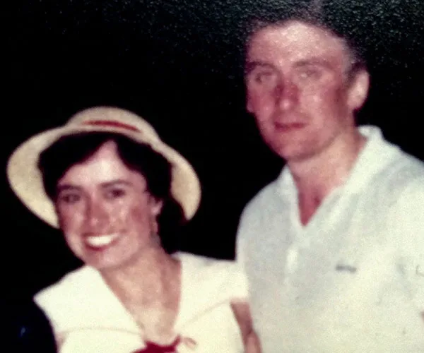 Two people posing for a photograph; the woman is wearing a hat and the man is in a white shirt, smiling.