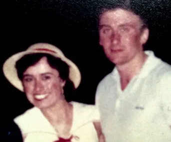 Two people posing for a photograph; the woman is wearing a hat and the man is in a white shirt, smiling.