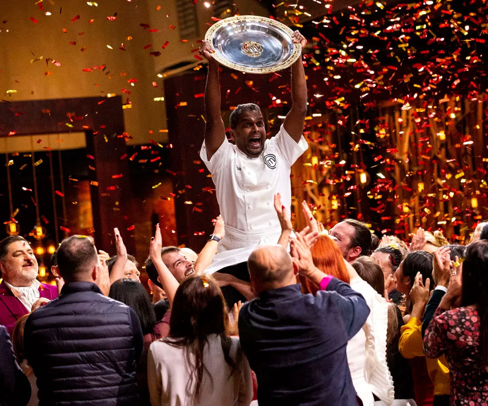 Sashi Cheliah celebrates winning MasterChef Australia 2018, holding trophy amidst cheering crowd and confetti.