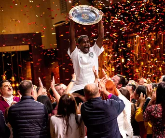 Sashi Cheliah celebrates winning MasterChef Australia 2018, holding trophy amidst cheering crowd and confetti.