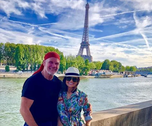 Couple posing by the Seine River with the Eiffel Tower in the background on a sunny day in Paris.