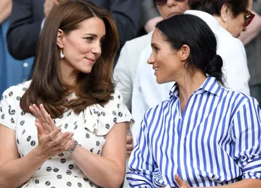 Two women smiling and talking at an outdoor event, surrounded by people.