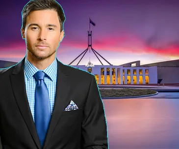 Man in a suit stands in front of the Australian Parliament House at sunset.