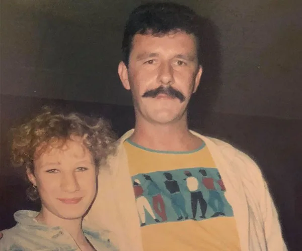 A man with a mustache and a woman with curly hair smiling, captured in a casual setting.