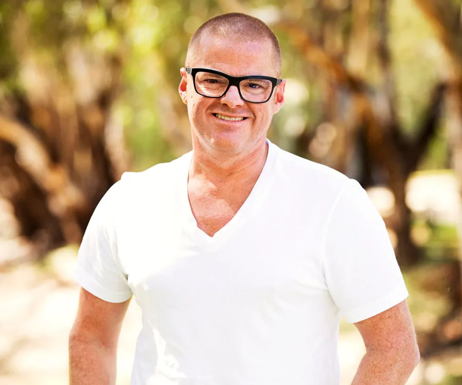 Man in glasses and white shirt smiling outdoors.