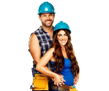 Couple wearing blue hard hats and tool belts, smiling, posing together.
