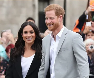 A smiling couple walking together outdoors, surrounded by a crowd.