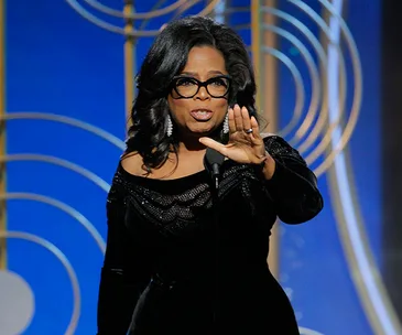Oprah Winfrey delivering a powerful speech at an awards ceremony, wearing a black dress and statement earrings.