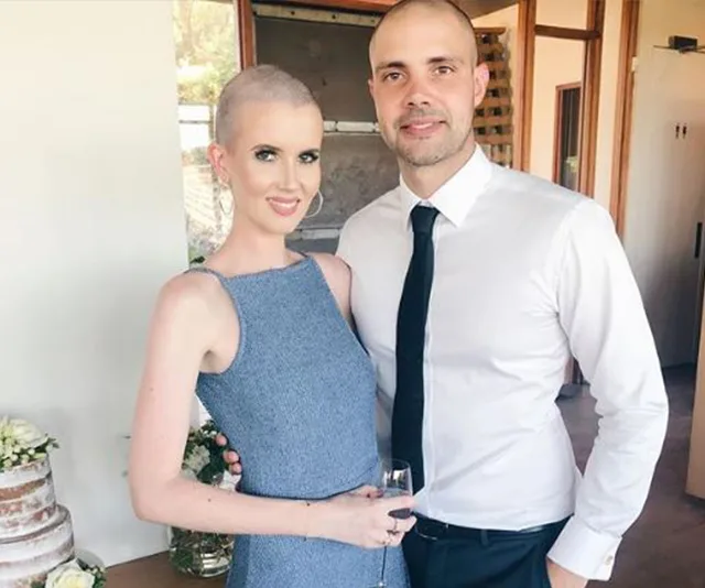 A couple posing together; the woman in a blue dress holds a drink, and the man wears a white shirt with a black tie.