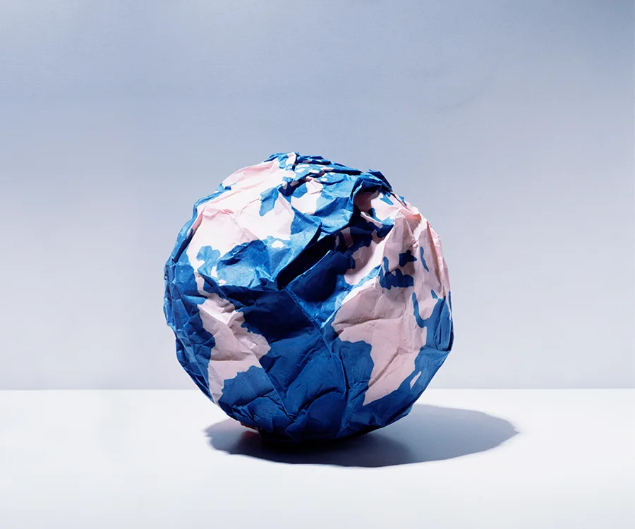 A crumpled paper globe with blue and pink continents against a soft gradient background.