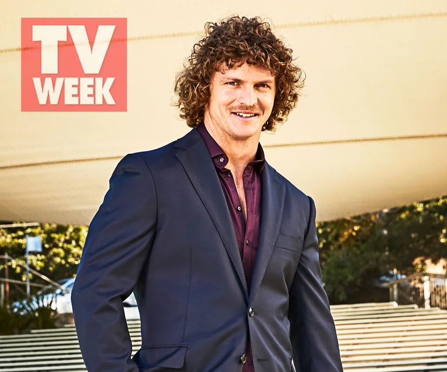 Man with curly hair and mustache in a suit, standing outdoors. TV Week logo in the top left corner.