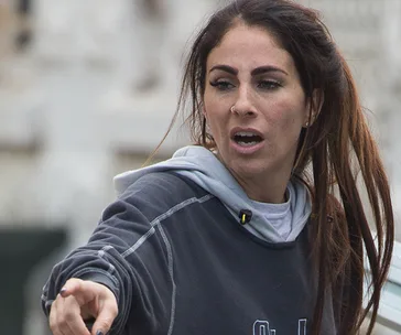 A woman with long hair and a nose ring pointing while wearing a hoodie, appearing to speak or argue outdoors.