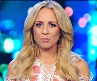 ```html
<img src="carrie-bickmore-breaks-down-50489.jpg" alt="Person with long blonde hair speaking on a TV show, wearing a floral dress." />
```