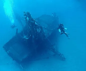 Divers exploring a sunken shipwreck on the ocean floor, with marine life beginning to cover the structure.