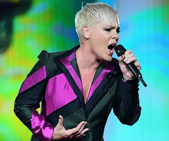 Singer wearing a pink and black outfit passionately performing on stage with a microphone.
