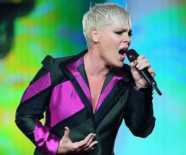 Singer wearing a pink and black outfit passionately performing on stage with a microphone.
