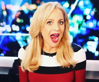 Blonde woman with open mouth, in black and red outfit against a colorful blurred background.
