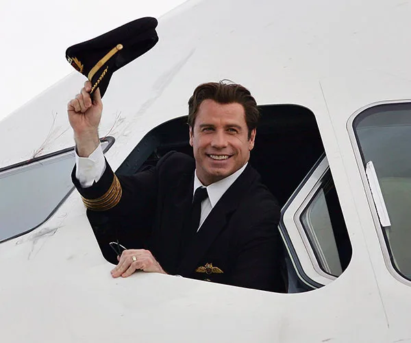 Pilot smiling and tipping hat from airplane cockpit window.