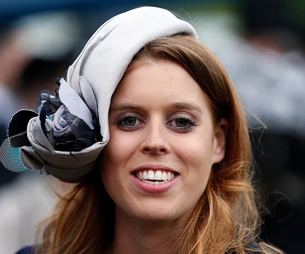 A woman with long hair wearing a decorative fascinator smiling at an outdoor event.