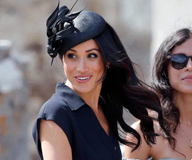 A woman in a stylish black dress and fascinator smiles while looking to the side, with another woman in sunglasses nearby.