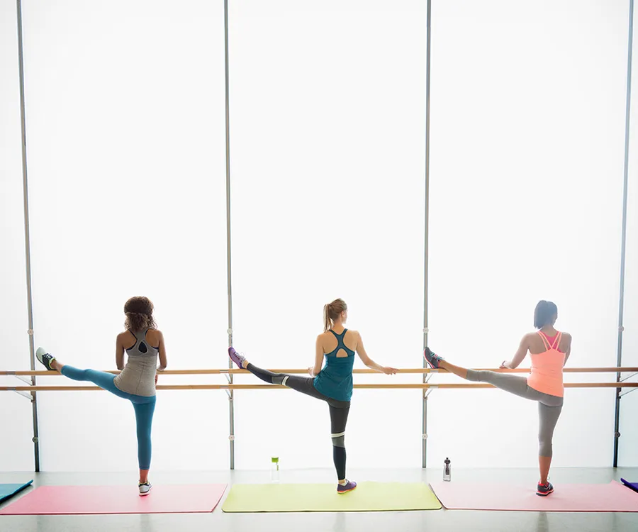 Women stretching at a barre in a bright fitness studio.